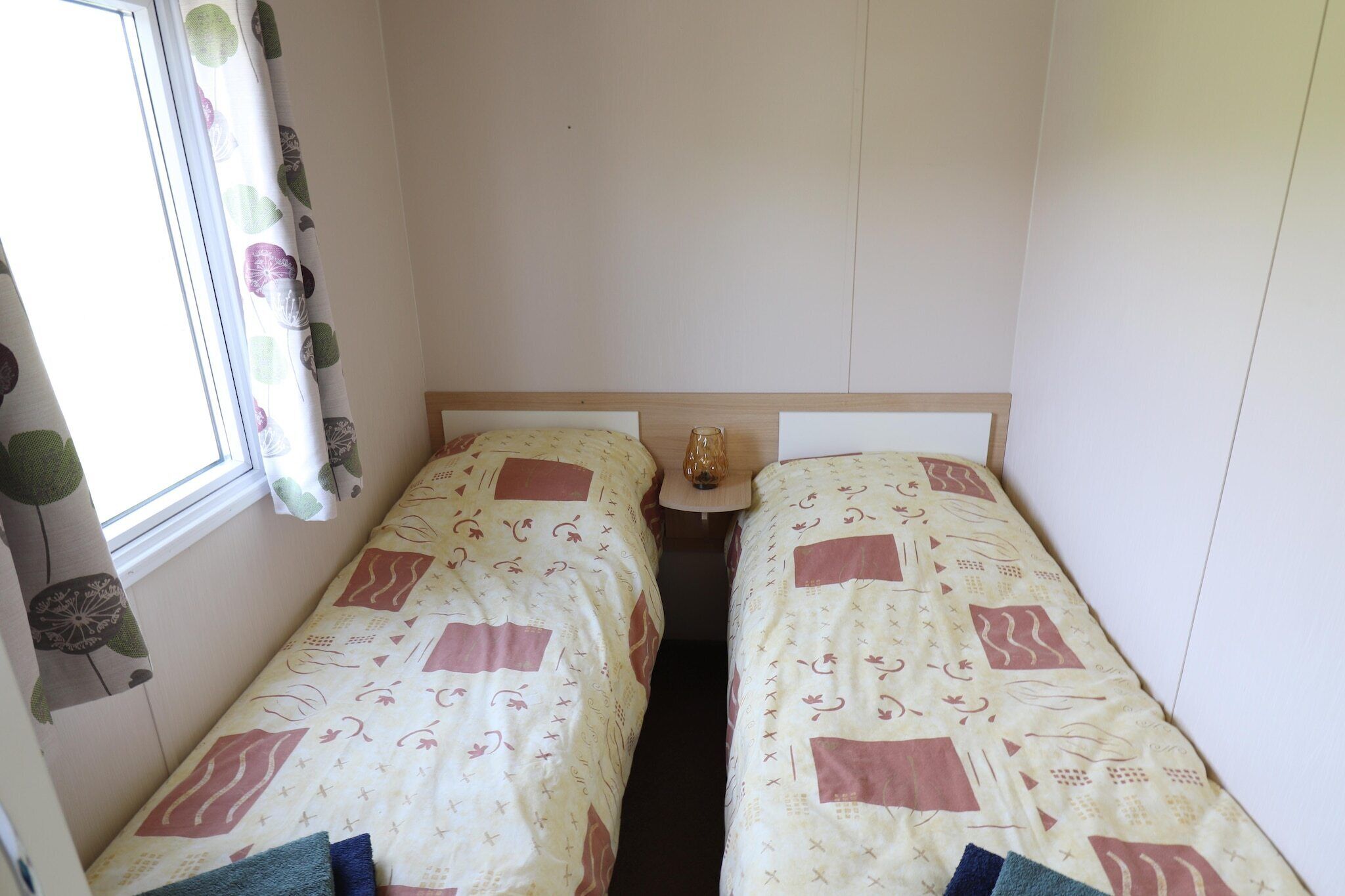 A small room with two single beds, a window with curtains, and a small table between the beds.