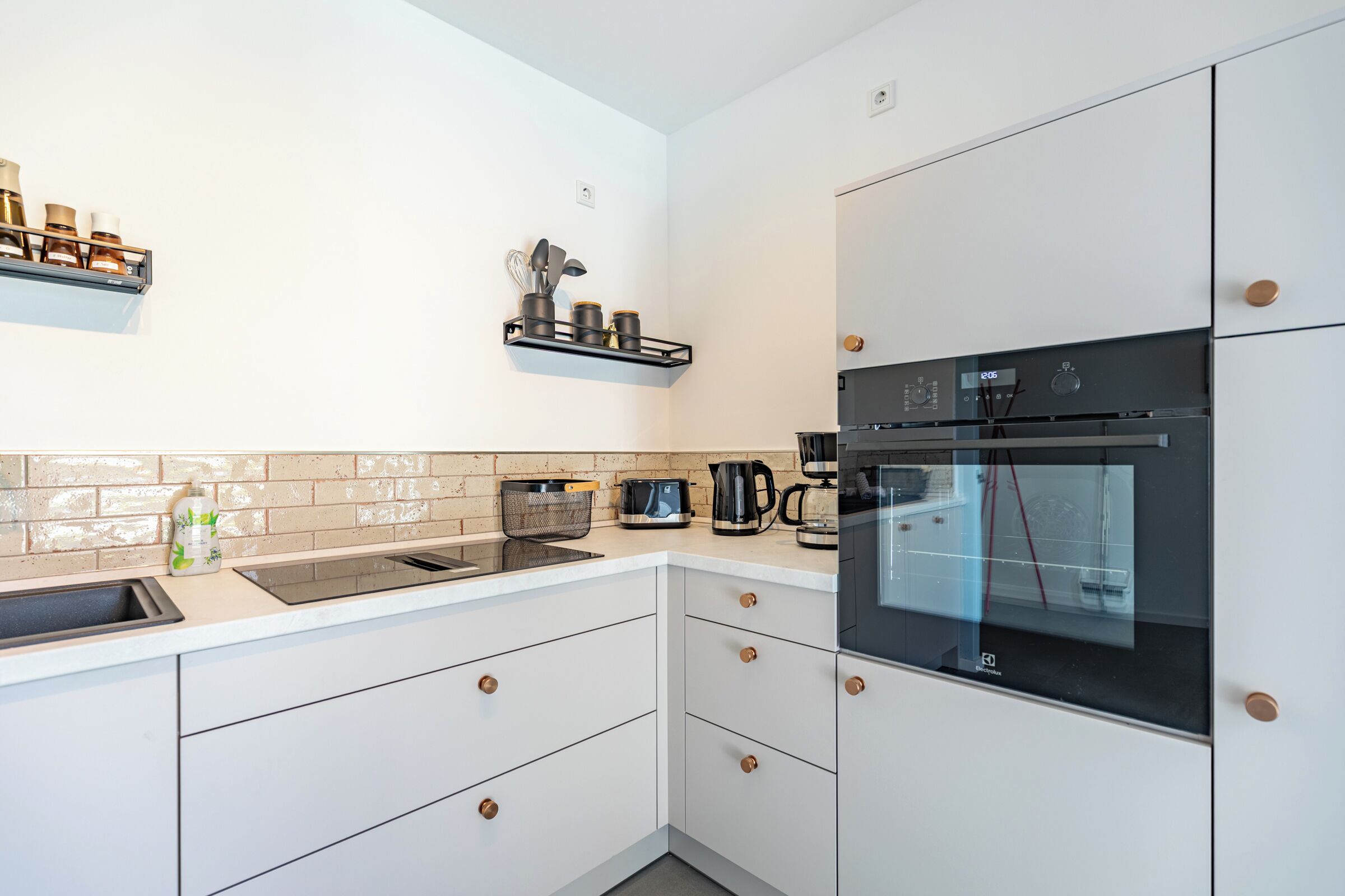 A modern kitchen with white cabinets, a black oven, and a stainless steel sink.