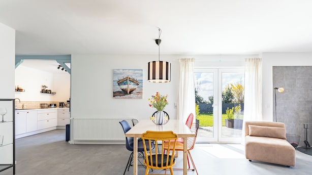 A modern kitchen with white cabinets, a dining table with chairs, a pendant light, and a painting of a boat on the wall. - Mareile: Vacation home for 6 people with terrace, WLAN and garden, 900 m to the sea (Uelvesbüll)