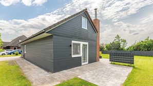 A modern two-story house with a dark exterior, a chimney, and a paved driveway. - Mareile: Vacation home for 6 people with terrace, WLAN and garden, 900 m to the sea (Uelvesbüll)