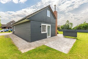 Ein modernes, zweistöckiges Haus mit dunkler Fassade, einem Schornstein und einem gepflasterten Auffahrt.
