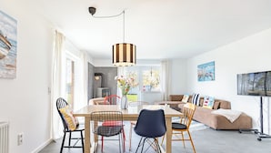 A modern living room with a dining area, a sofa, and a TV. - Mareile: Vacation home for 6 people with terrace, WLAN and garden, 900 m to the sea (Uelvesbüll)