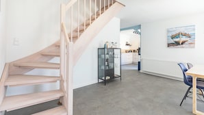 A modern interior with a wooden staircase, a kitchen area, and a dining table with chairs. - Mareile: Vacation home for 6 people with terrace, WLAN and garden, 900 m to the sea (Uelvesbüll)