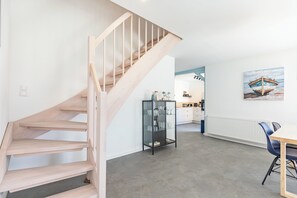 Ein modernes Interieur mit einer Holztreppe, einer Küchenzeile und einem Esstisch mit Stühlen.