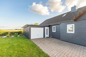 A modern house with a grey exterior, a white garage door, and a brick patio. - Cottage "Cottage am Deich Whg. (Uelvesbüll)