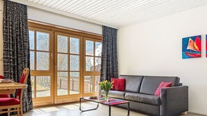 Ein Wohnzimmer mit einer Couch, einem Couchtisch, einem Sessel und einem Fenster mit Vorhängen.