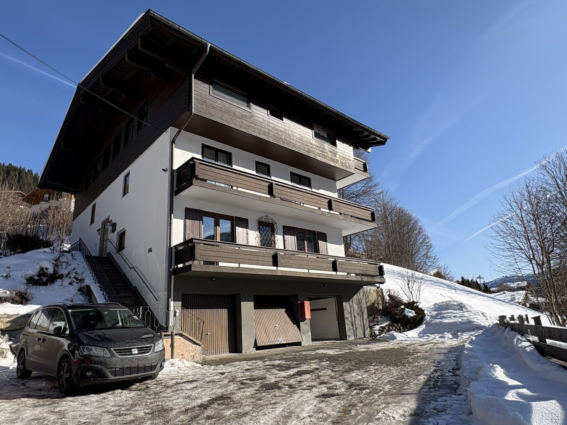 Un edificio de varios pisos con un coche estacionado frente a él, rodeado de nieve.