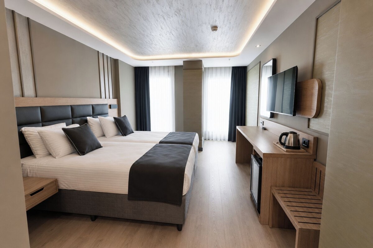Een moderne hotelkamer met een groot bed, een bureau met waterkoker en een flatscreen televisie aan de muur.
