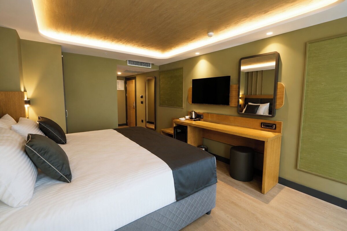 Een hotelkamer met een bed, bureau, televisie en een spiegel.