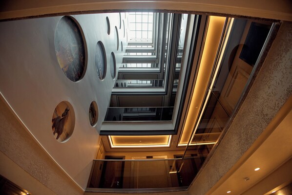 Ein modernes Interieur mit Glasdecke, geometrischen Wandmustern und einer zentralen Treppe.