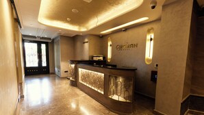 Ein Hotel-Rezeptionsbereich mit Marmorboden, einem Empfangstresen mit Glastrennwand und einem an der Wand befestigten Schild.