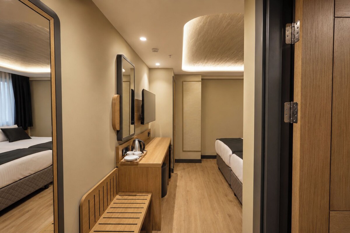 A compact hotel room with a bed, a small desk with a mirror, a bedside table, and a wardrobe.