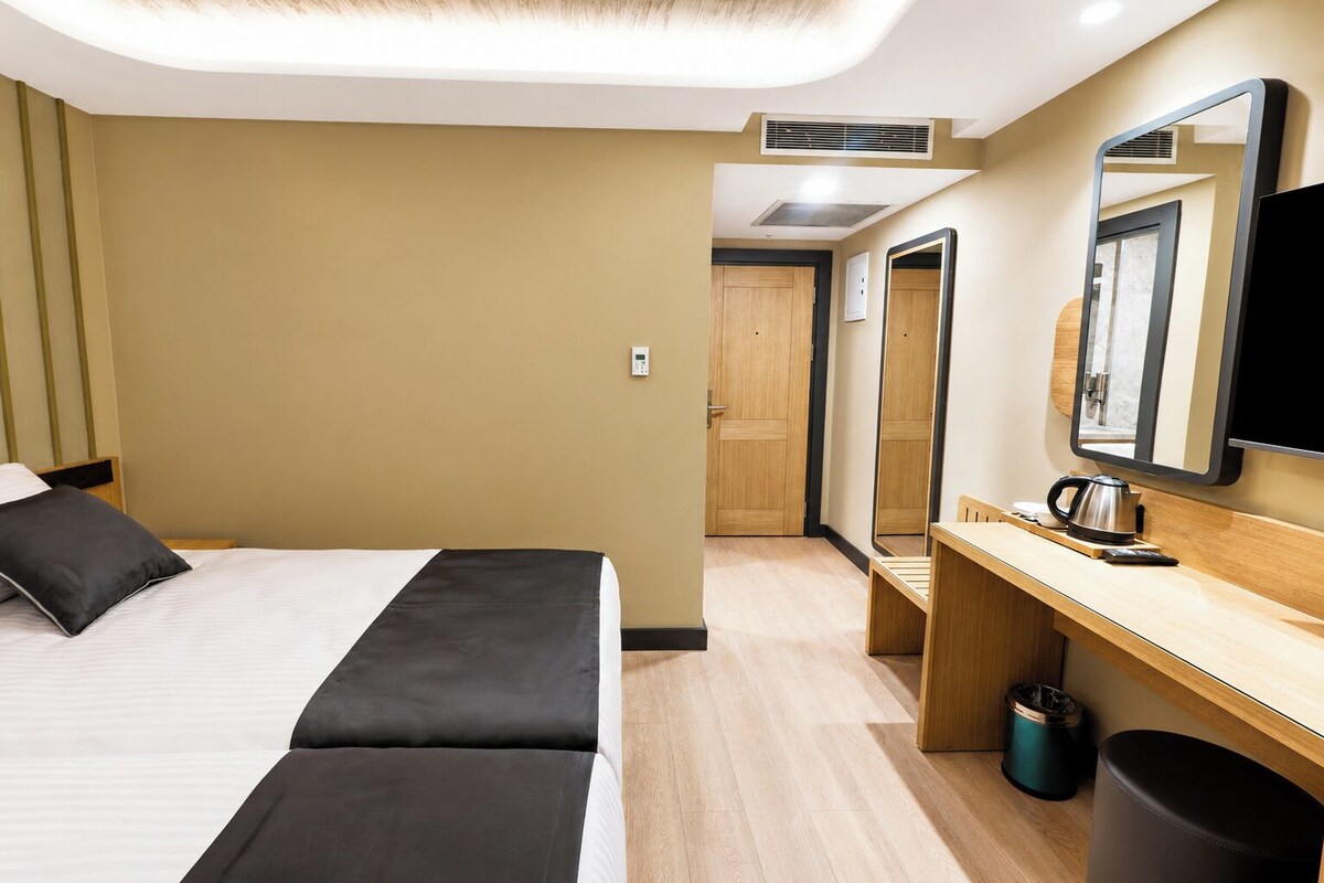Habitación de hotel con cama, escritorio, espejo, televisor y cesto de basura.