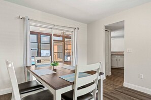 A dining area with a wooden table, white chairs, and a view through a glass door to a kitchen. - Siesta Key Pool BBQ Mini Putt 3BR 2BA Sleep 12 (Palmetto)