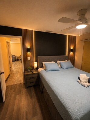 A bedroom with a bed, bedside tables, a ceiling fan, and a door leading to another room. - Spacious 4BR 2 BA Private Backyard Sleep 10 (Palmetto)