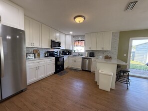 A modern kitchen with white cabinets, stainless appliances, and a central island. - Spacious 4BR 2 BA Private Backyard Sleep 10 (Palmetto)
