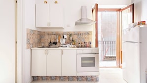 Una cucina compatta con pensili bianchi, forno integrato, macchina per il caffè e diverse spezie sul piano di lavoro.