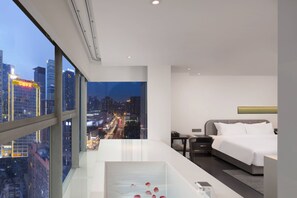 A modern hotel room with a large window, a bed, a bedside table, and a glass coffee table with rose petals. - Laizhu Xingchen Hotel  (Chengdu)