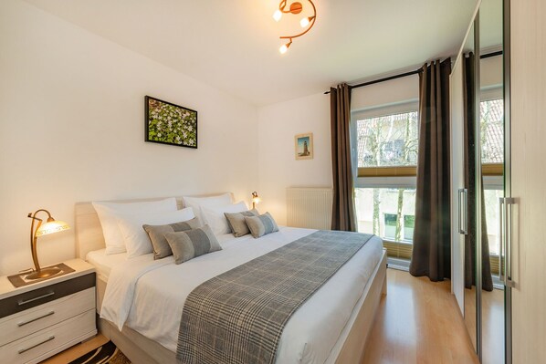 Ein Schlafzimmer mit Bett, Nachttischen, einer Lampe, einem Fenster mit Vorhängen und einem Wandbild.