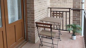 Un balcon avec des murs en briques, une porte en bois et une table en métal avec des bancs.
