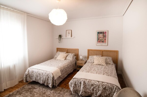 Une chambre double avec deux lits, un luminaire suspendu, un tableau encadré et une petite plante.