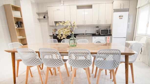 Une cuisine moderne avec des meubles blancs, une table à manger en bois et six chaises, ainsi qu’un vase rempli de fleurs.