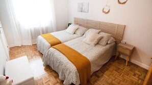 Un lit double avec une couvre-lit à motifs et un plaid de couleur moutarde, une table de chevet avec une radio et une couronne décorative accrochée au mur.