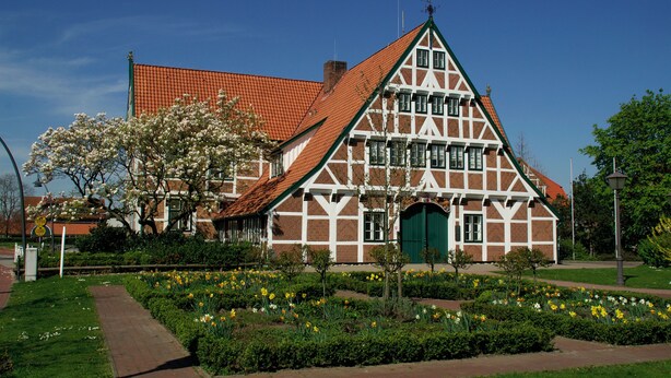 Una casa tradicional con entramado de madera y una puerta verde, rodeada de un jardín bien cuidado con plantas en flor.