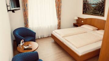 A hotel room with a bed, a TV mounted on the wall, a desk with a lamp, and a painting on the wall.