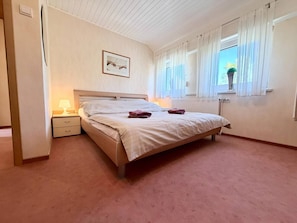 Une chambre à coucher avec un lit, une table de chevet, une lampe et une fenêtre avec des rideaux.