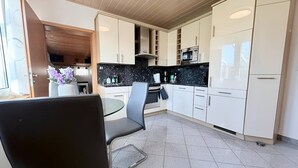 Moderni keittiö, jossa on valkoiset kaapit, musta työtaso sekä ruokailutila, jossa on lasipöytä ja -tuolit.