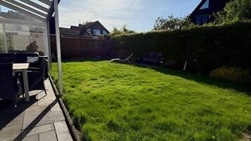 Ein gepflegter Garten mit einer Terrasse, einem Rasen und einem Haus im Hintergrund.