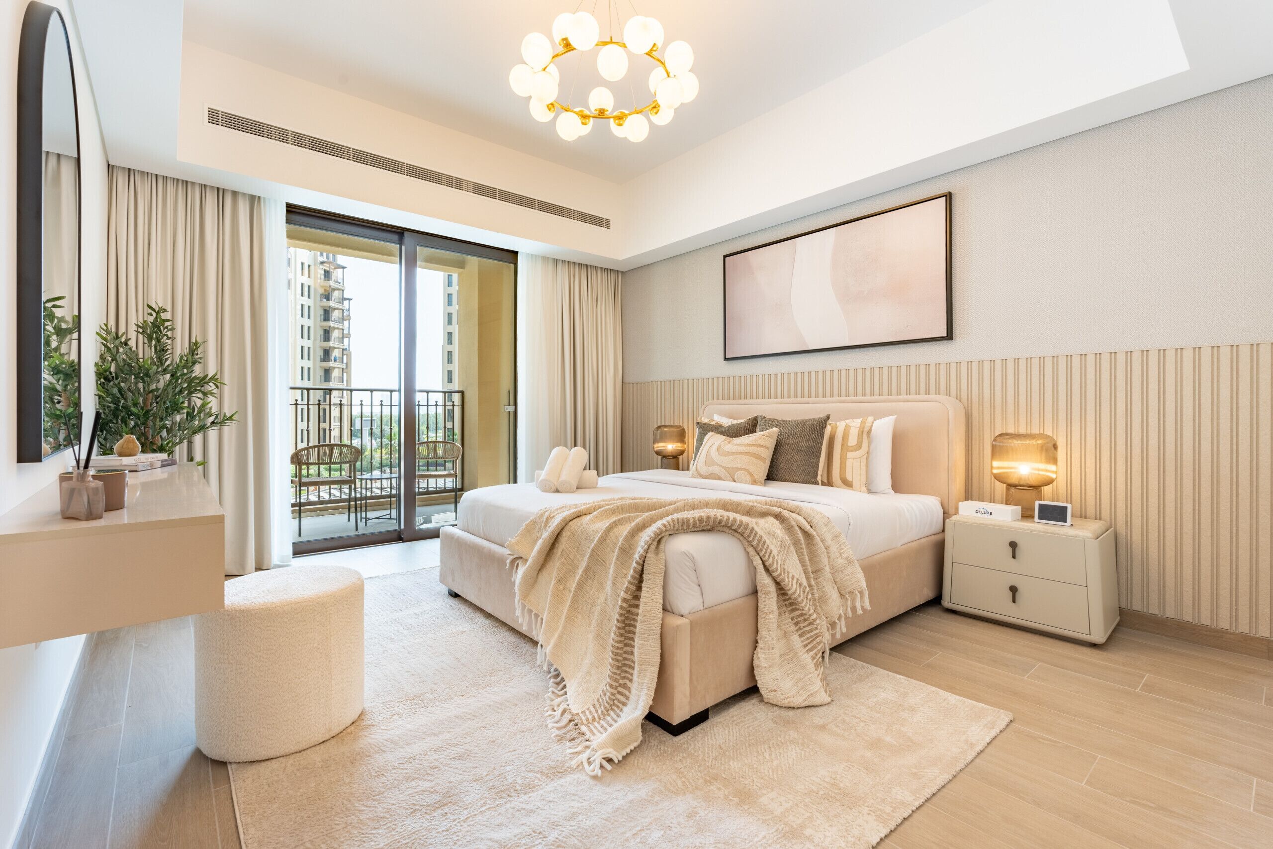 Een moderne slaapkamer met een groot bed, nachtkastjes, een spiegel en een balkon met uitzicht op hoge gebouwen.