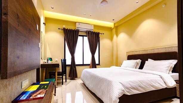 Una habitación de hotel con una cama, un escritorio, aire acondicionado y una ventana con cortinas.