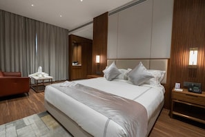 Habitación de hotel con una cama grande, cabecera de madera, un escritorio con teléfono y un sillón rojo.