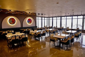A modern dining area with round tables and chairs, large windows, and a polished floor. - Hotel Park Central  (Ahilyanagar)