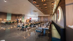 Ein geräumiges Restaurant mit modernem Design, das einen langen Essbereich mit Tischen und Stühlen, eine Bar und eine dekorative Decke mit runden Leuchten bietet.