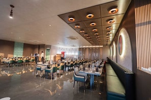 A spacious restaurant with a modern design, featuring a long dining area with tables and chairs, a bar area, and a decorative ceiling with circular light fixtures. - Hotel Park Central  (Ahmednagar)