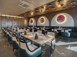 A modern restaurant with long tables, chairs, and a ceiling with circular light fixtures. - Hotel Park Central  (Ahilyanagar)