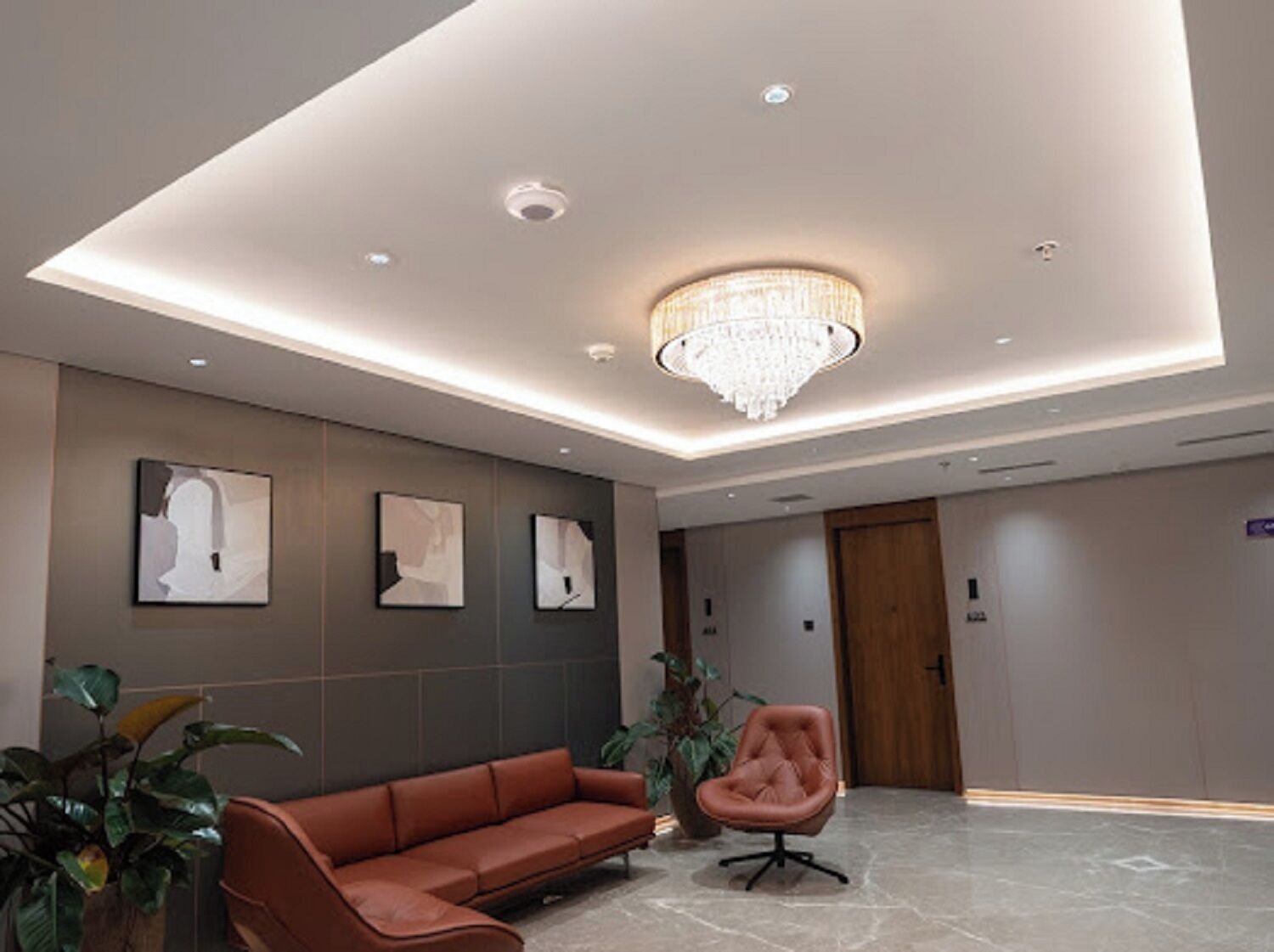 A modern lobby with a chandelier, a brown leather sofa, and abstract wall art.
