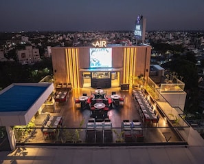 Un bar en la azotea con una pantalla grande, mesas al aire libre y vistas panorámicas de la ciudad.
