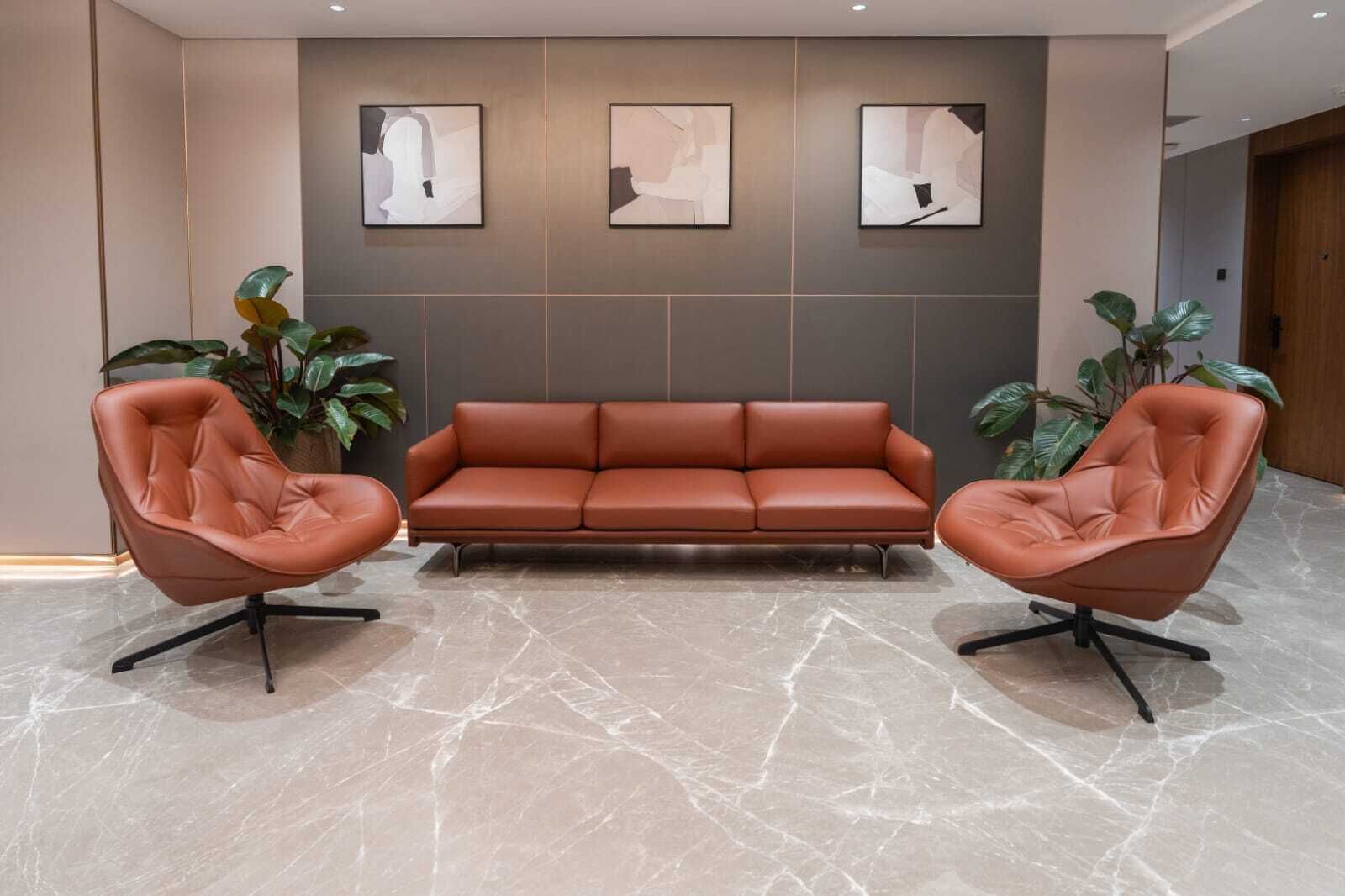 A modern lobby with a leather sofa, two leather armchairs, and abstract wall art.
