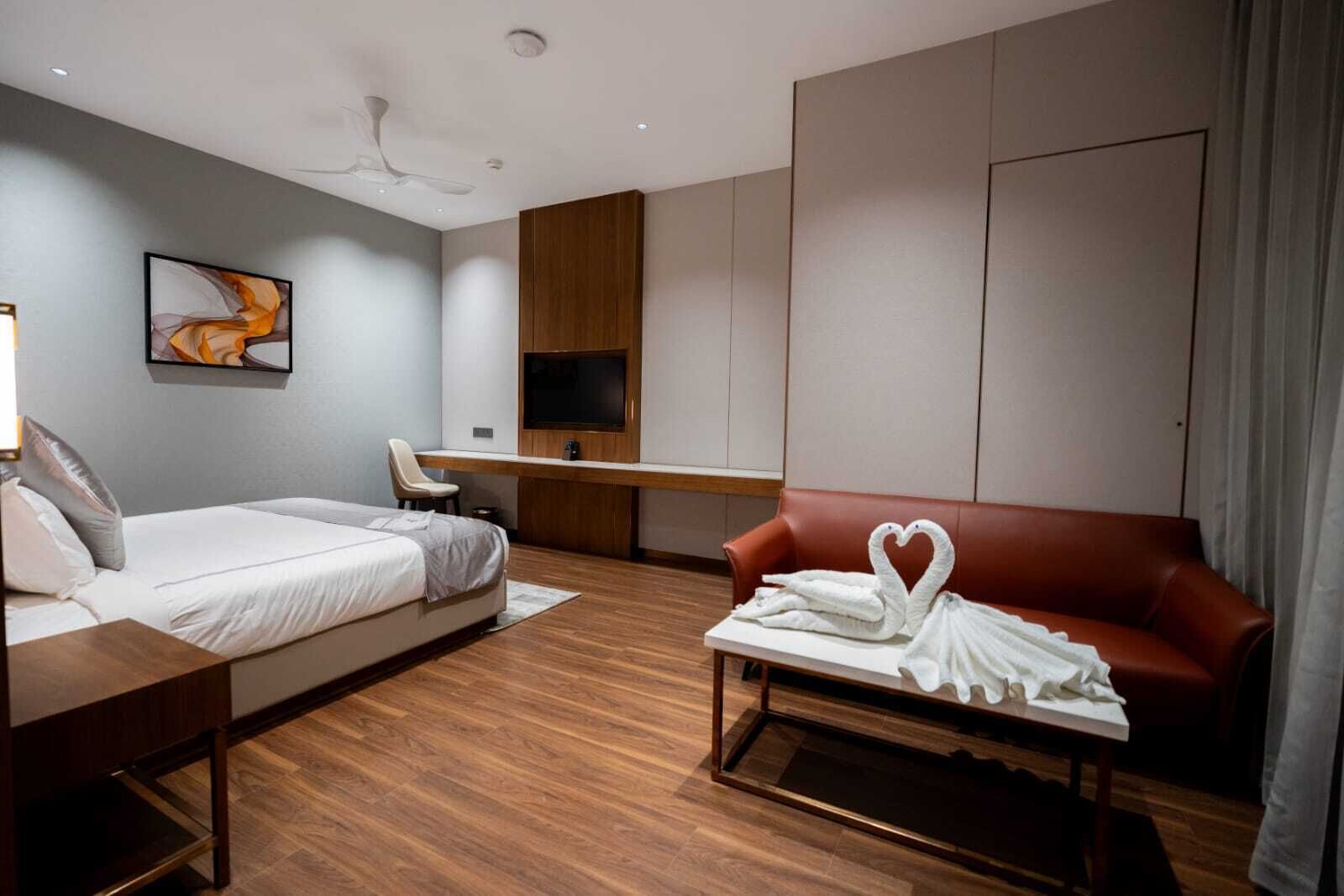 Una habitación de hotel con una cama, un escritorio, un televisor, un sofá y una decoración de toallas con forma de cisne.