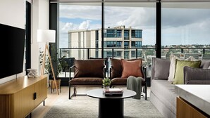 A modern living room with a sofa, armchair, and coffee table, large windows with a city view, and a flat-screen TV. - Elevated 3BR Stay - Views, Amenities, Parking (Newcastle West)
