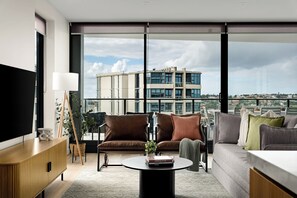 A modern living room with a sofa, armchair, and coffee table, large windows with a city view, and a flat-screen TV. - Elevated 3BR Stay - Views, Amenities, Parking (Newcastle West)