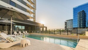 A rooftop pool with lounge chairs, a small table, and a glass building in the background. - Elevated 3BR Stay - Views, Amenities, Parking (Newcastle West)