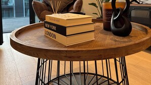 Une table ronde en bois, dotée d’un pied en métal noir, sur laquelle sont posés une pile de livres, une bougie et un objet décoratif.
