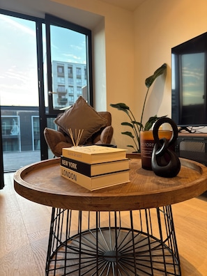 Ein runder Holztisch mit schwarzem Metallgestell, Bücherstapel, Kerze und ein dekorativer Gegenstand.
