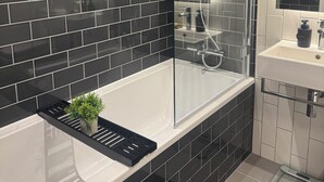 Une salle de bain moderne avec des murs recouverts de carreaux noirs, une douche en verre, une baignoire blanche et une petite plante en pot.