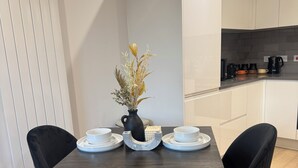 Une table à manger avec deux chaises, un vase contenant des fleurs séchées et une machine à café posée sur le comptoir.